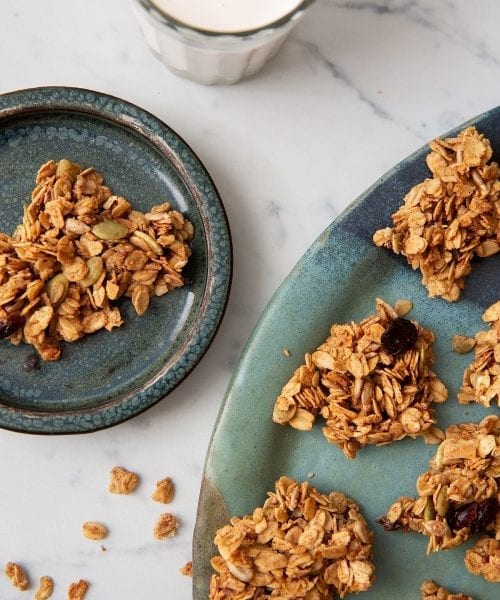 Chewy  Vanilla Granola Clusters on plates surrounded by a glass of milk